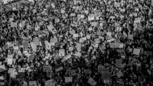 Juodai balta nuotrauka, vaizduojanti gausią minią žmonių su plakatais viešojo protesto metu.