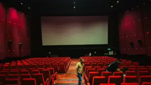 Tuščia kino salė su raudonomis kėdėmis priešais didelį kino ekraną.