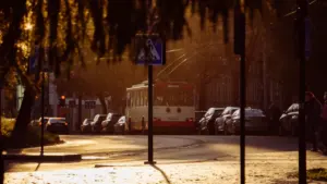 Raudonas troleibusas važiuoja Vilniaus gatve šviečiant saulės spinduliams.