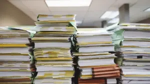 Didelės popierinių dokumentų krūvos ant stalo biure ruošiant finansines ataskaitas.