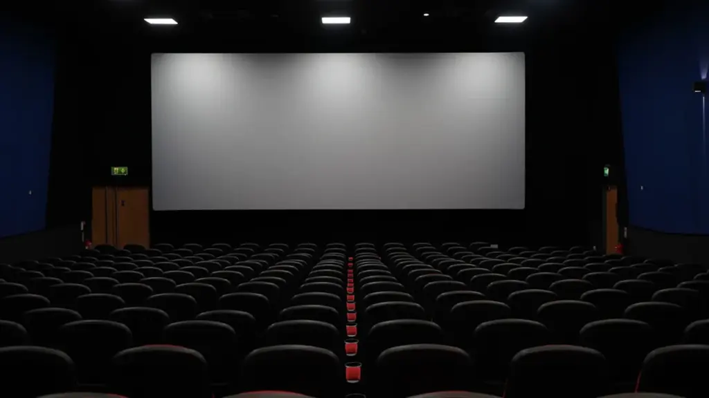 Tuščia kino salė su raudonomis kėdėmis ir baltu ekranu prieš kino seansą.