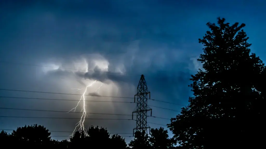 Elektros perdavimo bokštas audros metu su žaibo išlydžiu danguje virš medžių