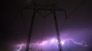 Elektros perdavimo bokštas audros metu su ryškiais žaibais tamsiame danguje.