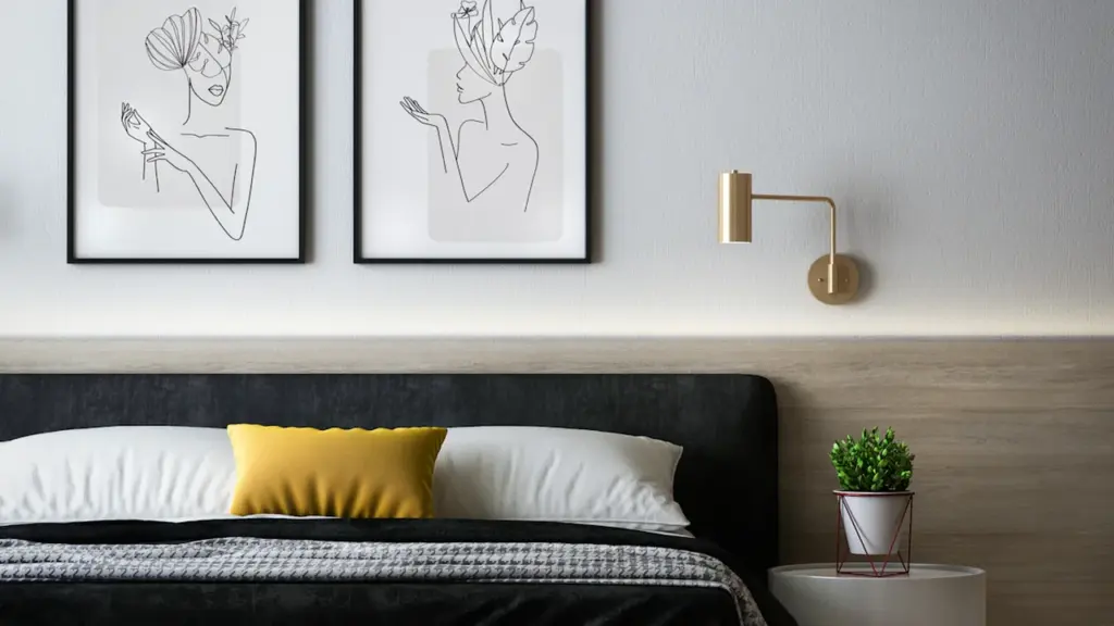 Moderni miegamojo siena su dviem minimalistiniais meno rėmeliais ir elegantišku apšvietimu.