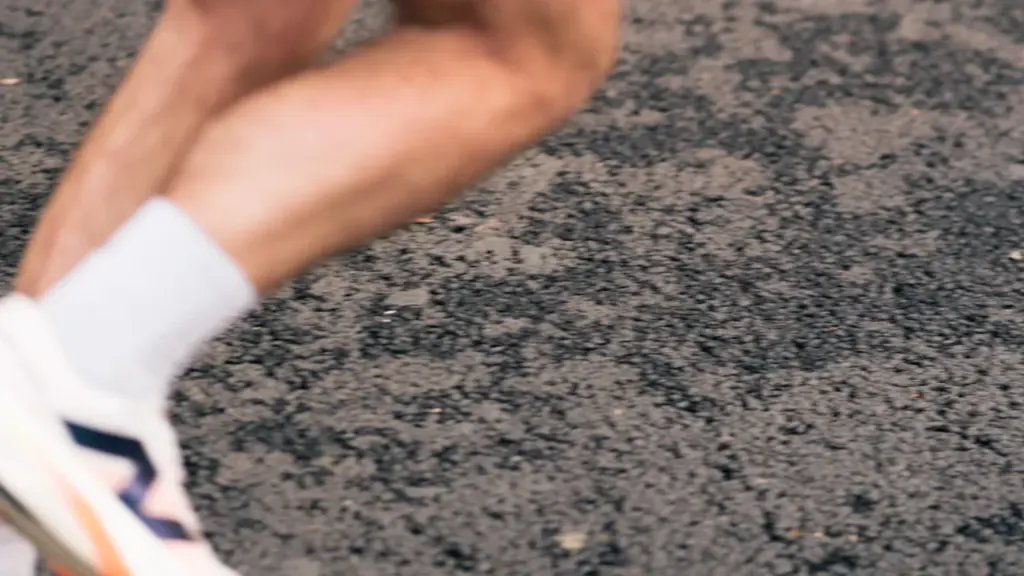 Bėgiko kojos sportiniuose bateliuose energingai juda asfaltuoto bėgimo takelio paviršiumi sportuojant lauke.