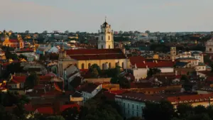Vilniaus senamiesčio panorama su bažnyčių bokštais ir raudonais stogais vakaro šviesoje.