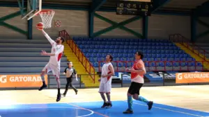 Krepšininkas atlieka metimą į krepšį sporto arenoje varžybų metu tarp dviejų komandų.
